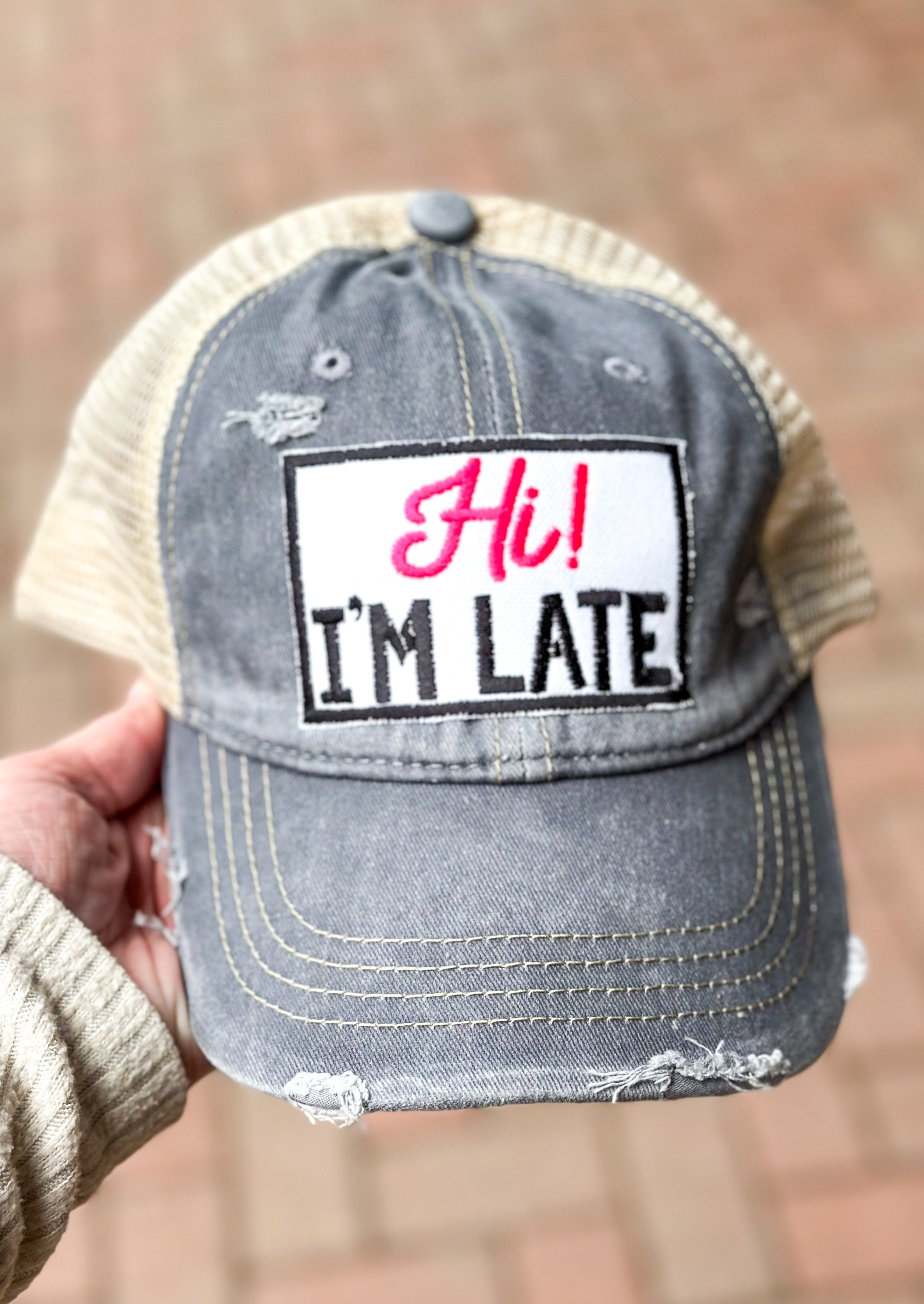 Gray distressed trucker hat with patch that says "Hi!" in hot pink and "I'm Late" in black