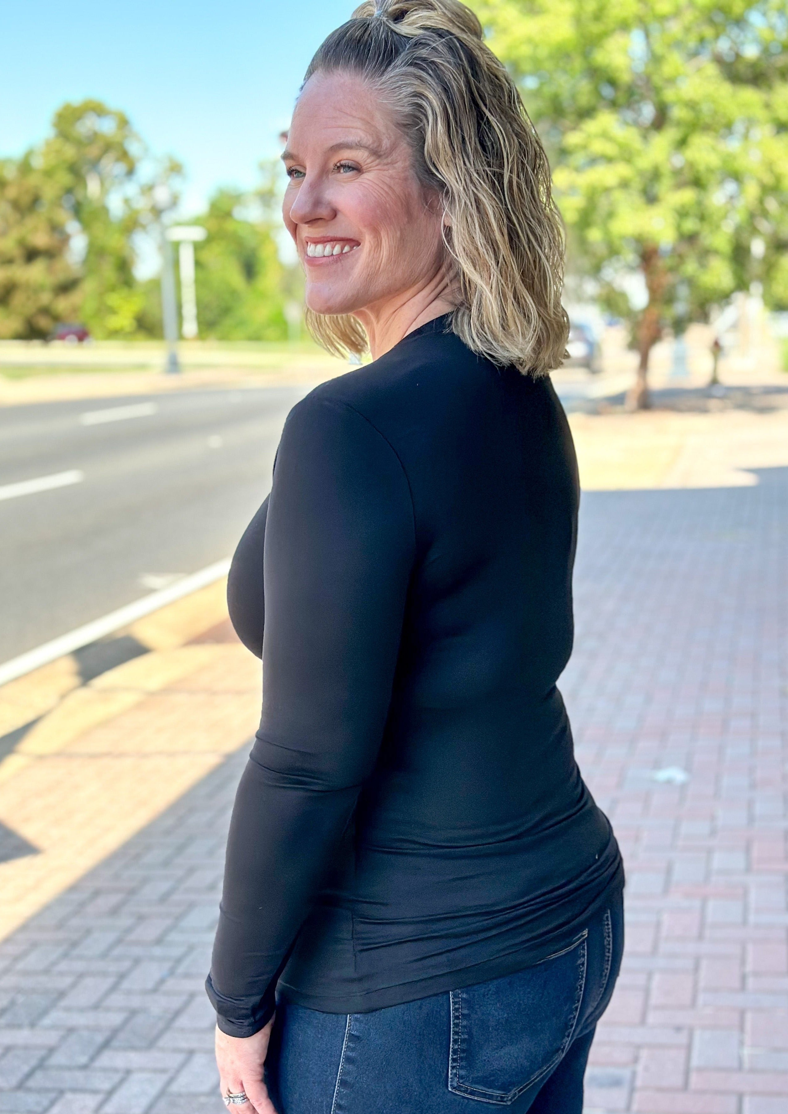 Side/back view of fitted black long sleeve top, has a little stretch and full coverage.