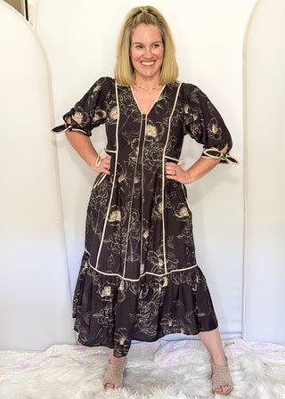 Black midi dress with cream piping and tie details on sleeves and waist.