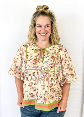 Soft floral Babydoll top with 3/4 puff sleeve, orange and green strip detail on banding of hem and sleeve. green ribbon detail on the front and tie at the collar.