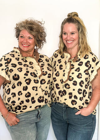 Beige short sleeve button-up blouse with bold black leopard spots and layered ruffle trim on the neckline and sleeves.