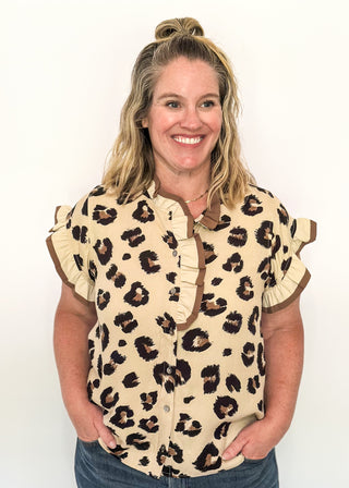 Beige short sleeve button-up blouse with bold black leopard spots and layered ruffle trim on the neckline and sleeves.