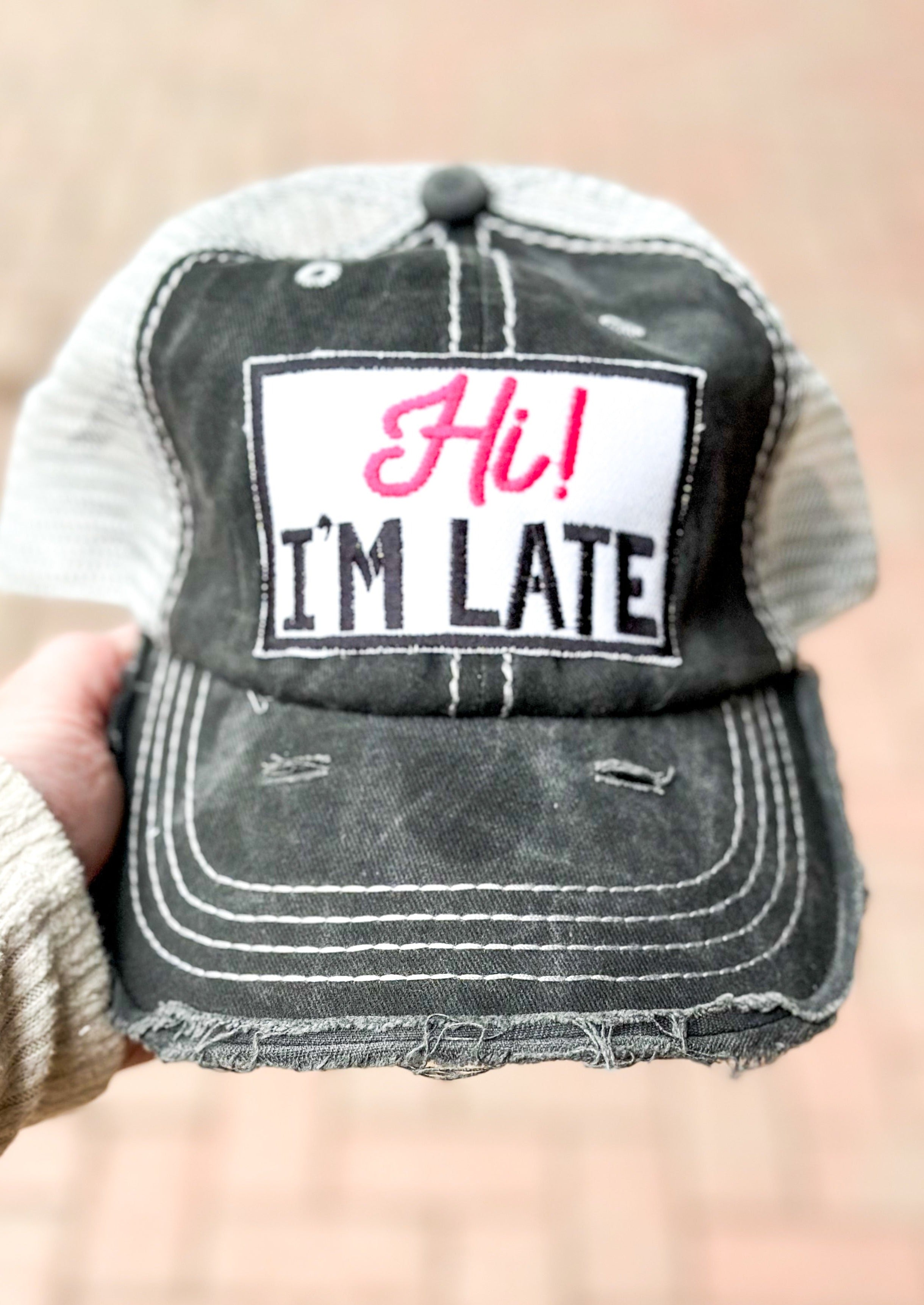 Charcoal trucker hat with white netting - patch attached that says Hi! I'm late.