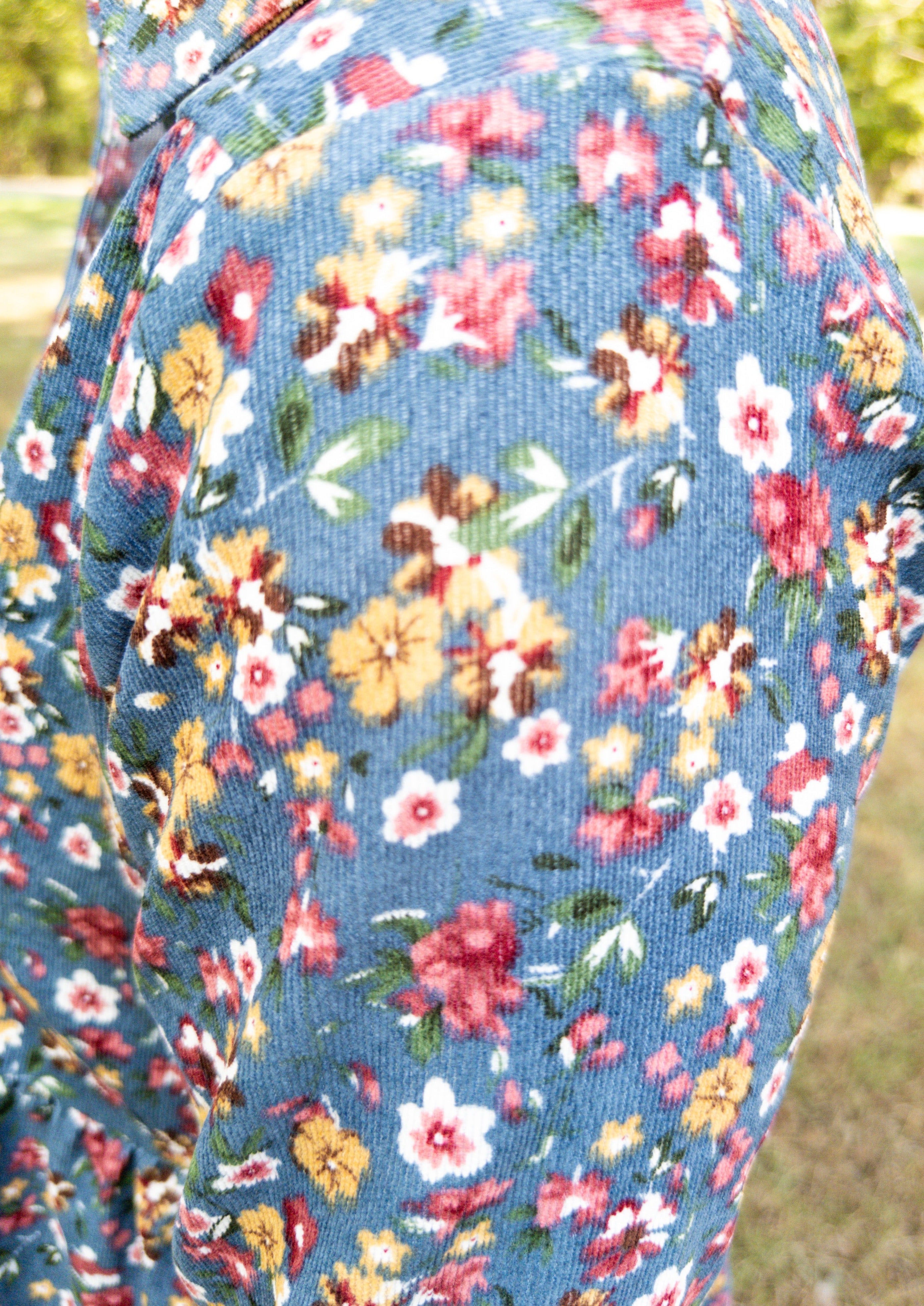 Close up side view of the dusty blue corduroy dress. It shows the texture from the corduroy and the pink, yellow, white, and green floral print.