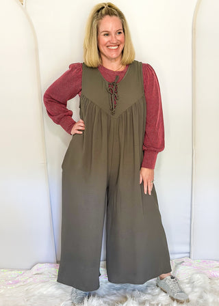 Charcoal gray sleeveless woven jumpsuit with ribbon tie neckline, pockets, and flowy wide-leg fit.