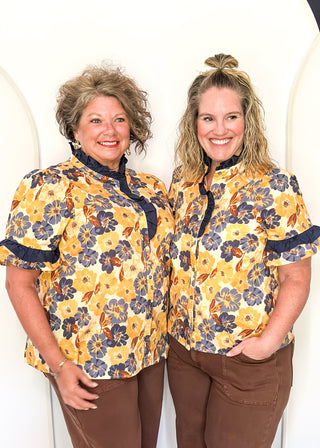Bold Navy and golden blooms on this short sleeve top with navy ruffle detail on the sleeves, collar and 1/2 way down the front. Buttons up the front.