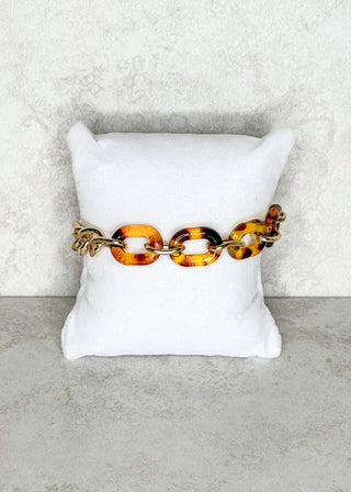 Tortoiseshell chain bracelet on a white pillow against a light gray background