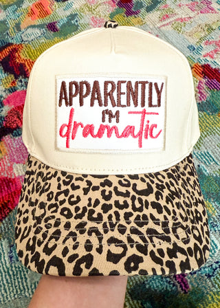Snapback canvas hat with natural canvas body, leopard print bill. Large white patch with "Apparently I'm (embroidered in black) dramatic" (embroidered in hot Pink)