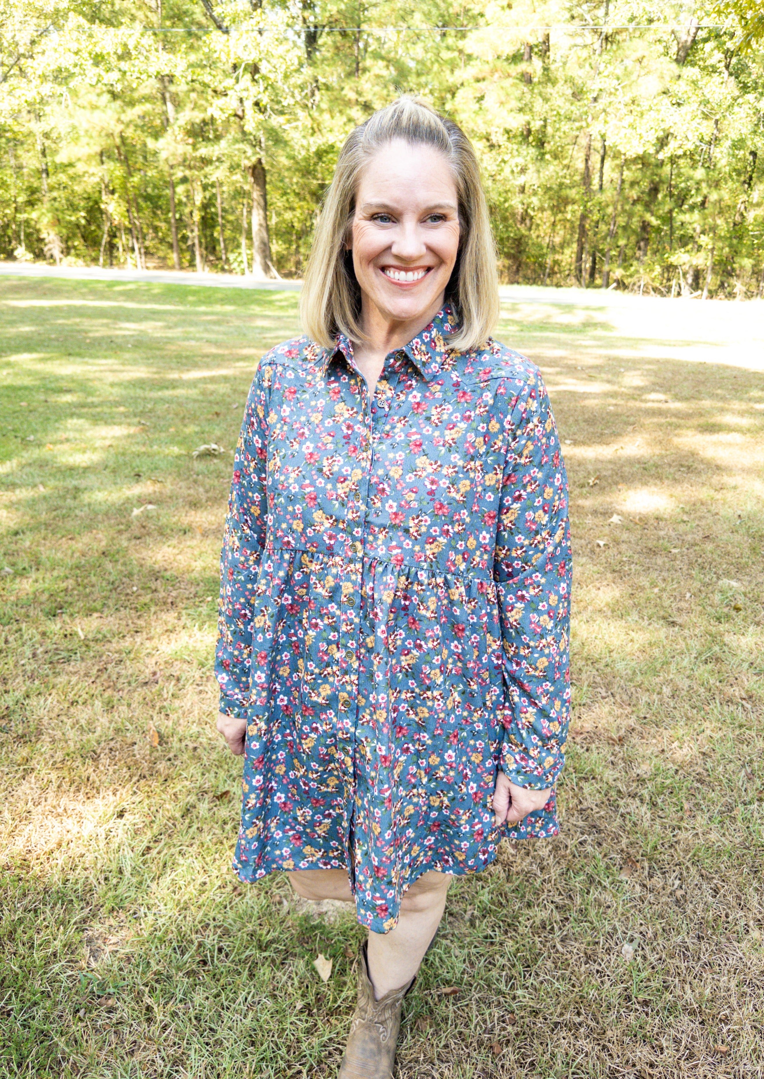 Dusty blue corduroy dress with long sleeves and a soft colored floral pattern all over. The dress has buttons all down the front and a collar.