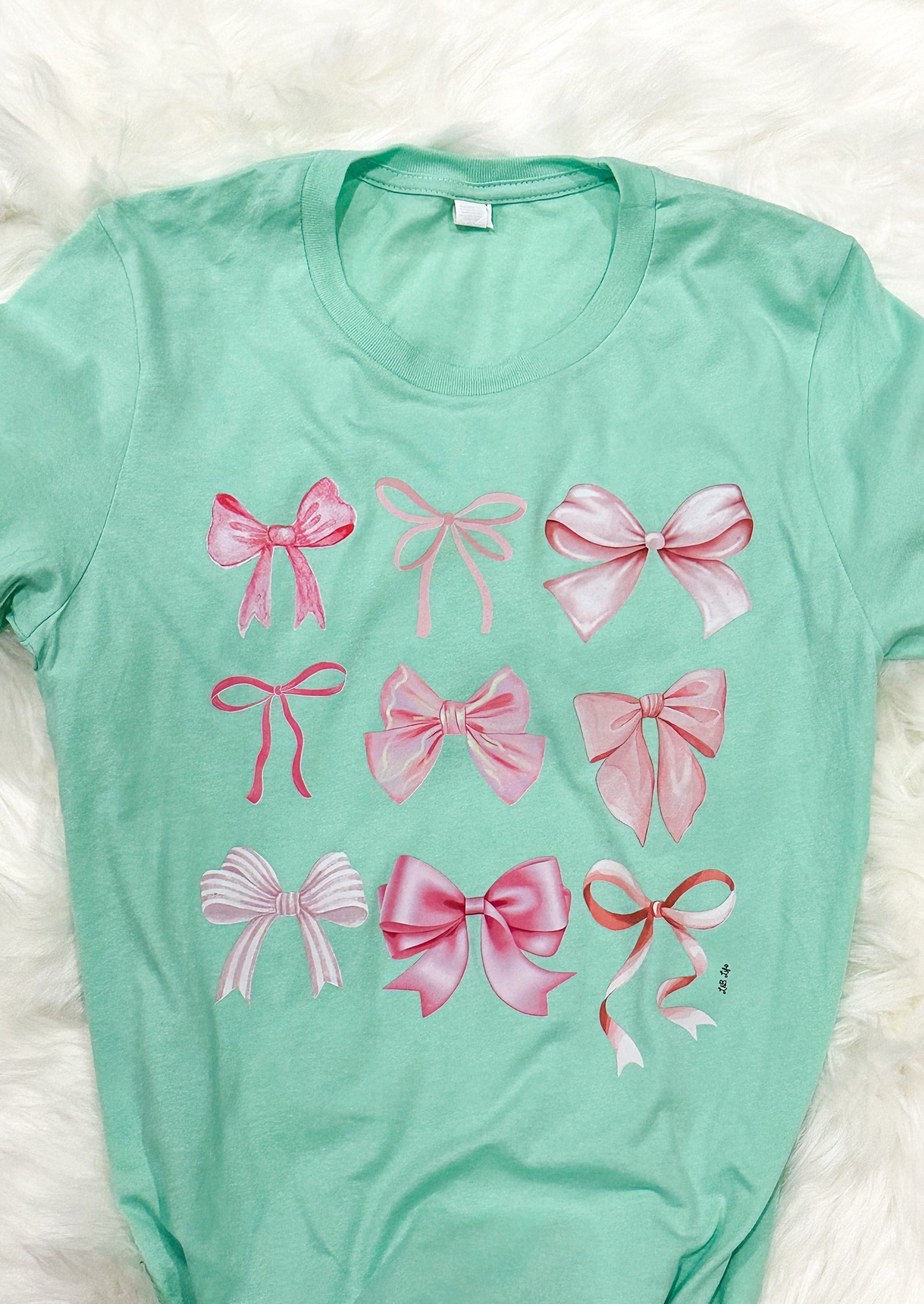 mint green Bella Canvas tee shirt with 9 different bows printed on it in pink