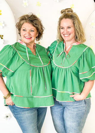 Green babydoll v-neck top with oversized balloon sleeve. multicolored piping detail on sleeve, hem, and collar.  Matching tie closure off of the collar.