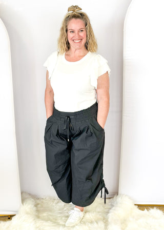 Solid black wide leg crop pants with pockets. Smocked waist with tie closure.  Ribbon cinch detail in the leg.
