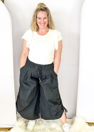 Solid black wide leg crop pants with pockets. Smocked waist with tie closure.  Ribbon cinch detail in the leg.