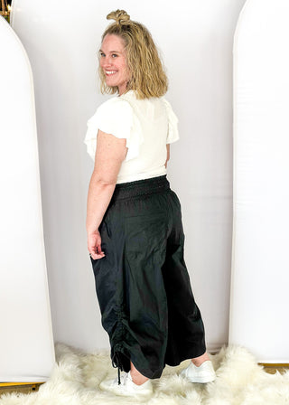 Solid black wide leg crop pants with pockets. Smocked waist with tie closure.  Ribbon cinch detail in the leg.