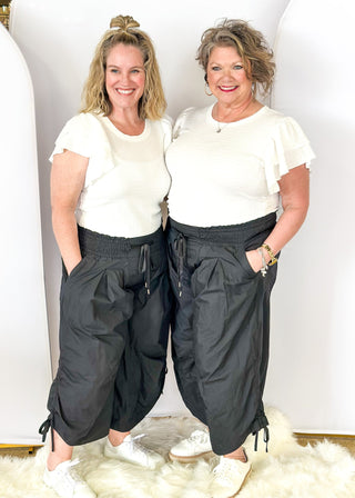 Solid black wide leg crop pants with pockets. Smocked waist with tie closure.  Ribbon cinch detail in the leg.