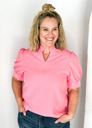 Pink short sleeve top with pearl detail on puff sleeves.  Ruffle collar with notched v-neck