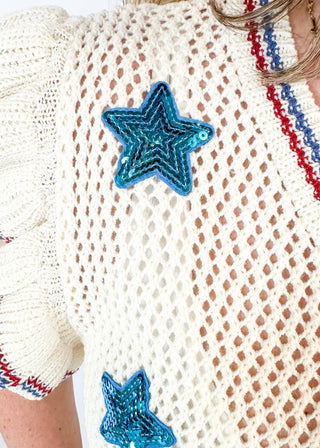 ruffle short sleeve net like cream sweater - need to wear something underneath - blue sequin star patches and red and blue trim around v-neck, bottom banding and ruffle on sleeve