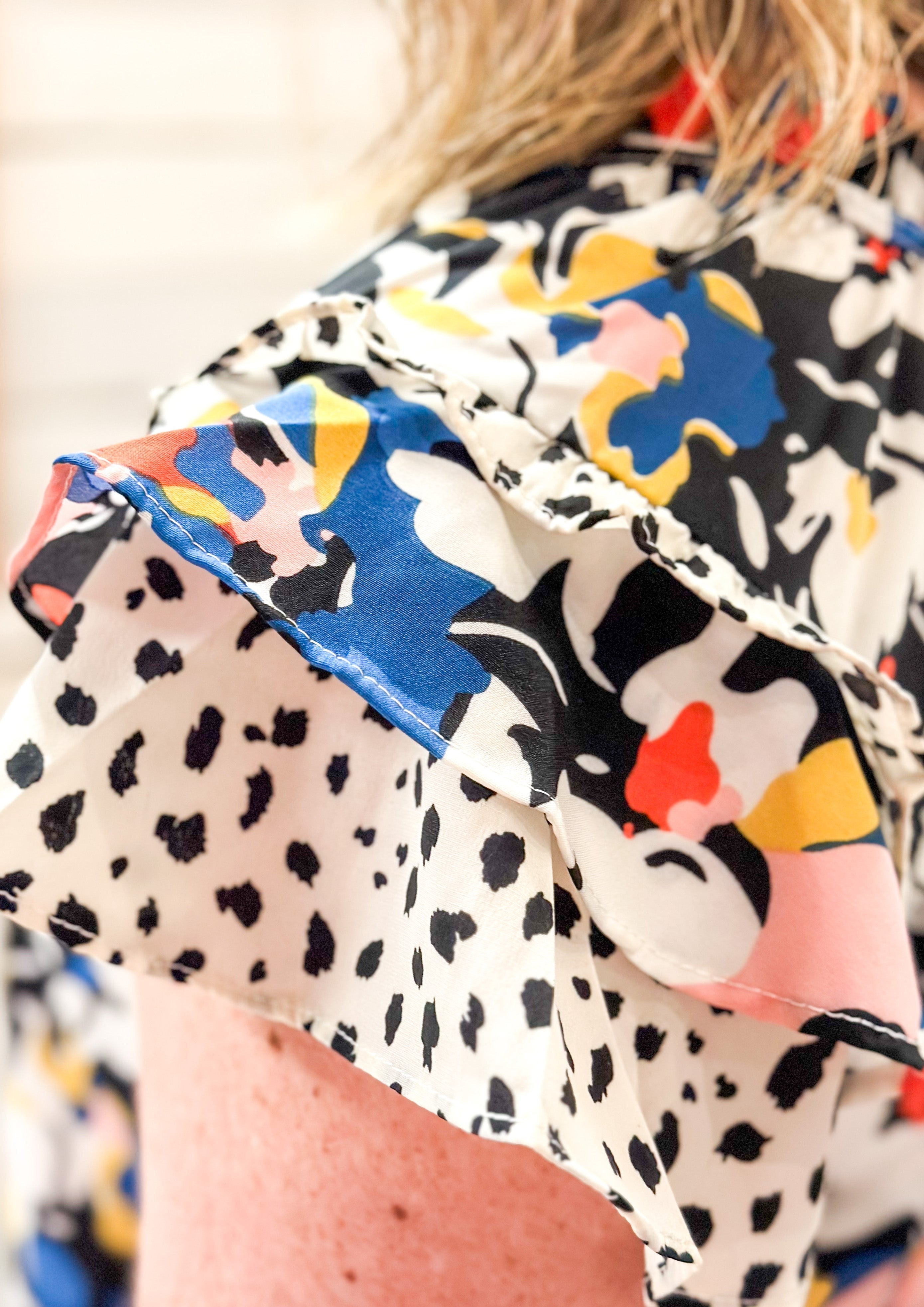 White pink blue yellow red and green flowers over black background. ruffle sleeve and neck with ties