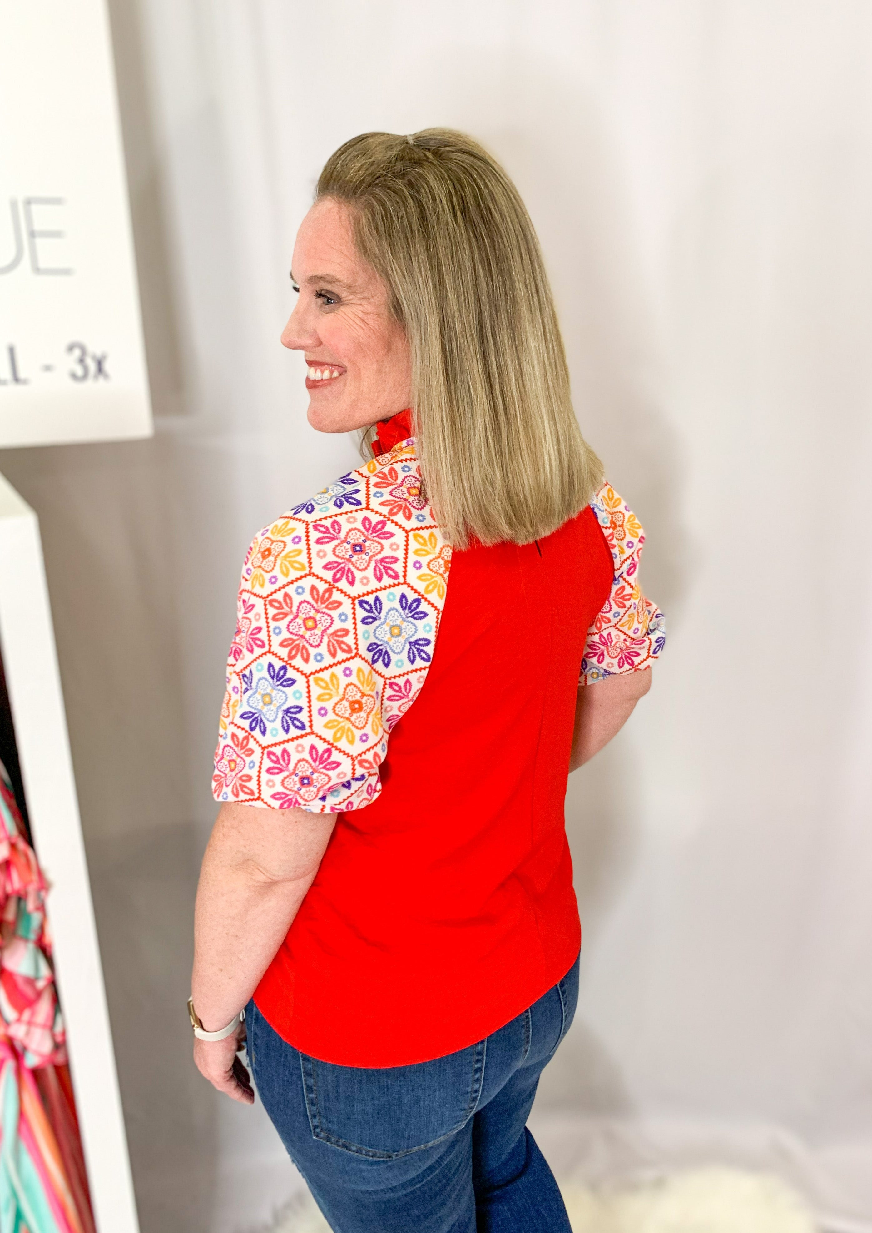Back/side view of Red top with a ruffle collar. White balloon sleeve with a multicolored printed embroidery pattern.