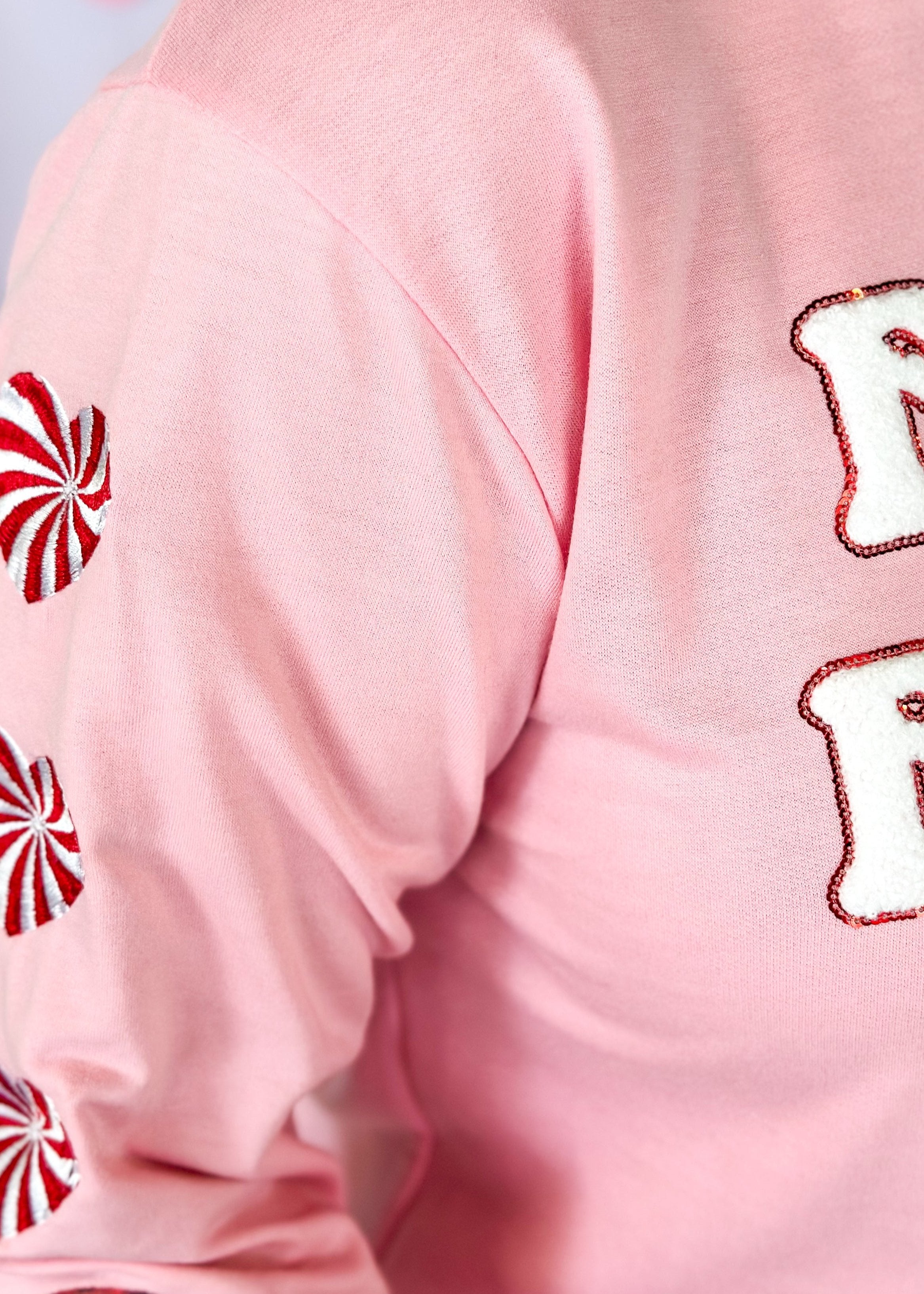 pink long sleeve top with feelin' festive patches across the front - heart shaped peppermint patches down the sleeve with one gingerbread man patch at the bottom of each sleeve