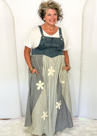 woman modeling a denim overall style dress with gingham floral pattern.