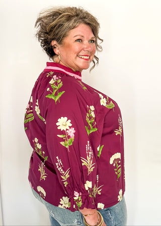 Plum top with florals in light pink and white with green leaves.  3/4 length sleeve and v-neck with contrast detail in plum and light pink. 