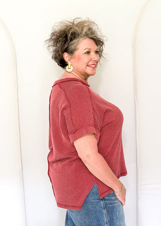Woman wearing a red textured shirt and blue jeans against a white background
