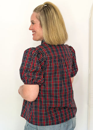 side view of woman wearing a plaid puff sleeve top in dark navy with short sleeves and a V-neckline.