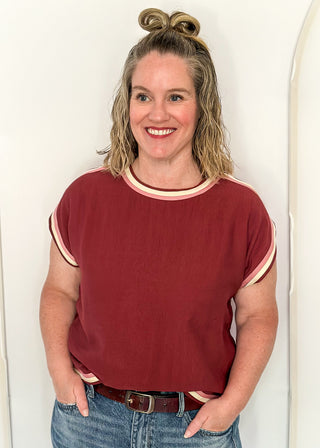 women wearing brick red top with cap sleeves and crew neckline, styled with jeans.