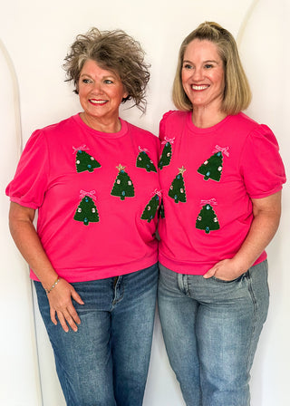 Two women wearing a short sleeve pink top with embellished mini trees.