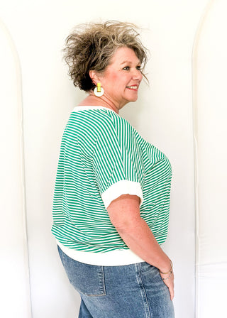 Woman wearing a green and white striped shirt and blue jeans against a white background