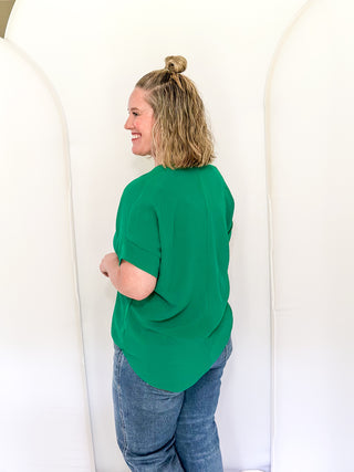 Woman wearing a green top and blue jeans standing against a white background
