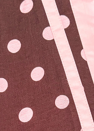 A close-up of a dark brown fabric with a pink polka dot pattern and a light pink striped border.