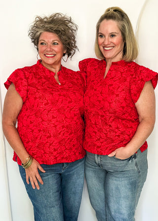Two women wearing red jacquard flutter sleeve blouses with a floral pattern, standing side by side.