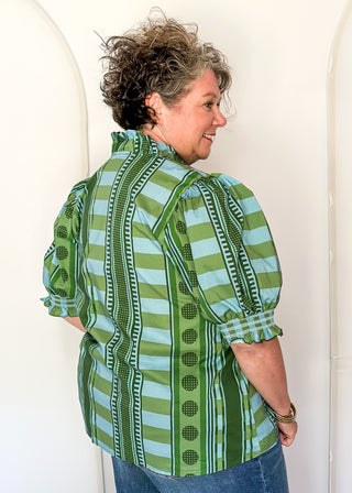 A woman wearing a green and light blue striped button-up shirt with puff sleeves, shown from the back against a white arched backdrop.