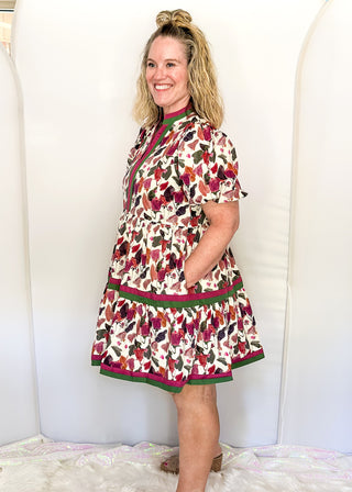 Short puff sleeve, tiered A line dress with plum, terracotta, and dark green florals. Trimmed in plum and dark green with a v-neck.
