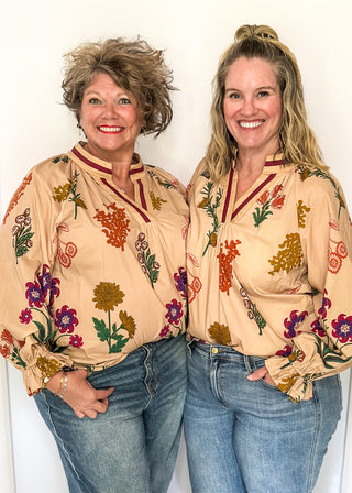 Beige top with v-neckline, contrast trim, and vibrant floral design.