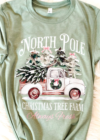 Green t-shirt with a Christmas-themed graphic of a truck and trees, labeled 'North Pole Christmas Tree Farm Always Fresh'.
