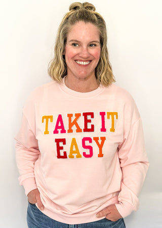Lightweight pink long-sleeve top with multicolor chenille patch letters spelling “TAKE IT EASY”