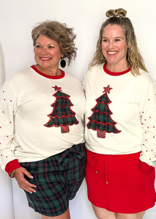 White long sleeve Christmas top with red neckline and cuffs, featuring a plaid Christmas tree appliqué with red sequin trim on the front. Red pearl accent the sleeves for a festive touch.”