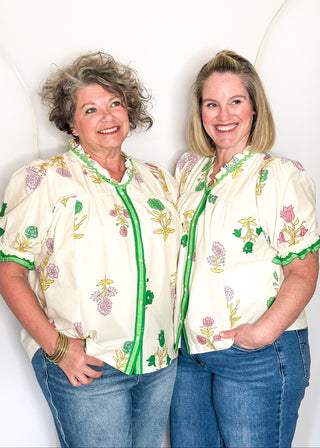 off white floral short sleeve button front blouse with pink and green flowers, featuring puff sleeves, ruffled neckline, and green trim.