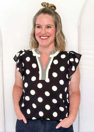 Women's black blouse with cream polka dots, striped split neckline, and flutter sleeves.