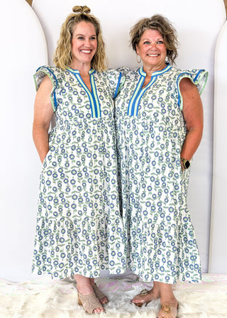 maxi dress with neutral background featuring mint and blue flowers and green stems/leaves - tiered - mint and blue ribbon trim around v-neckline  and collar - mint and blue trim around double ruffle sleeve - pockets