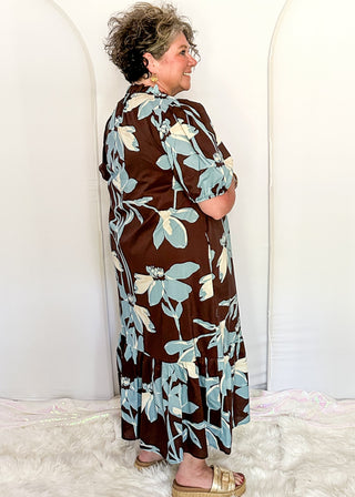 woman standing profile in a brown, soft blue and off white floral midi dress.