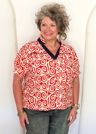 Red swirl print blouse with navy contrast trim, puff sleeves, and split neckline detail.