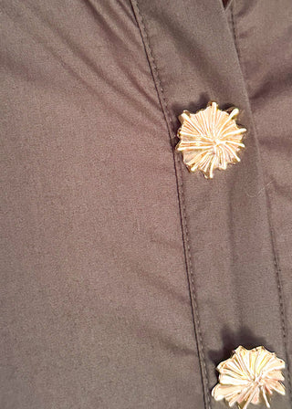 Close up of casual black women’s dress with collared neckline, rolled sleeves, and decorative gold snaps