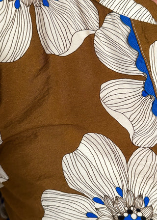 Close up of mocha colored floral blouse featuring white and blue blooms with blue scalloped trim. 