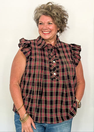 woman wearing a dark navy plaid top with flutter sleeves and rhinestone buttons.