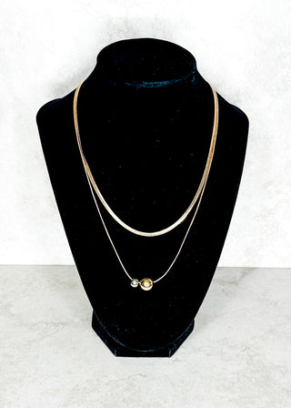 Gold necklace on a black mannequin bust against a white background