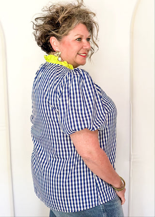 Women’s gingham blouse with decorative buttons and statement neckline detail.